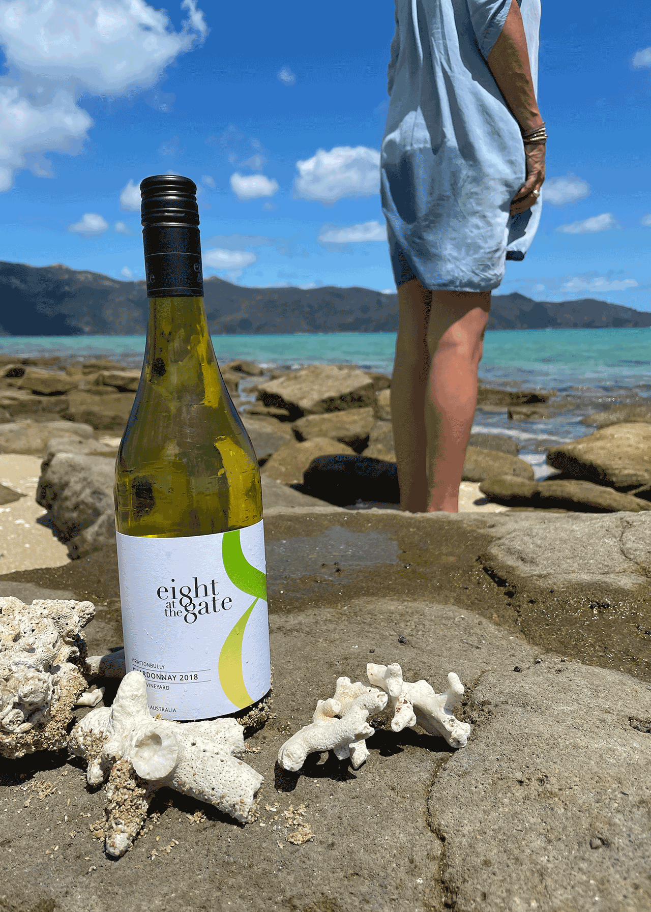 Eight at the Gate 2018 Chardonnay bottle at the beach with a person standing in the back facing the sea.